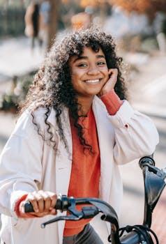 Cheerful woman with curly hair posing with her bicycle on a sunny day.