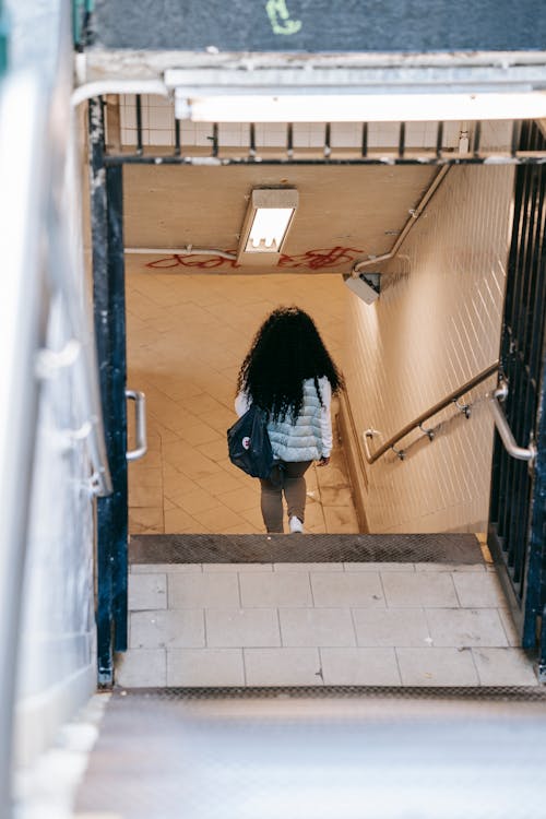 Back view anonymous female with long curly hair going downstairs in underground pedestrian passage