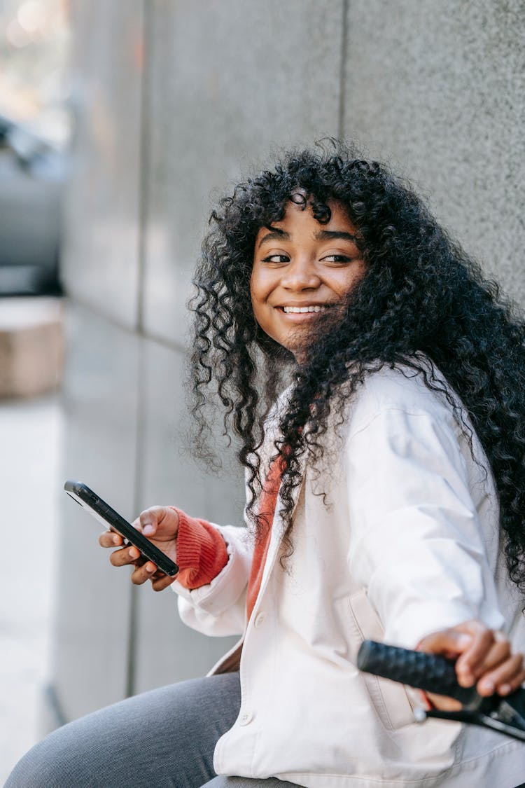 Cheerful Black Woman Sitting On Bicycle With Smartphone