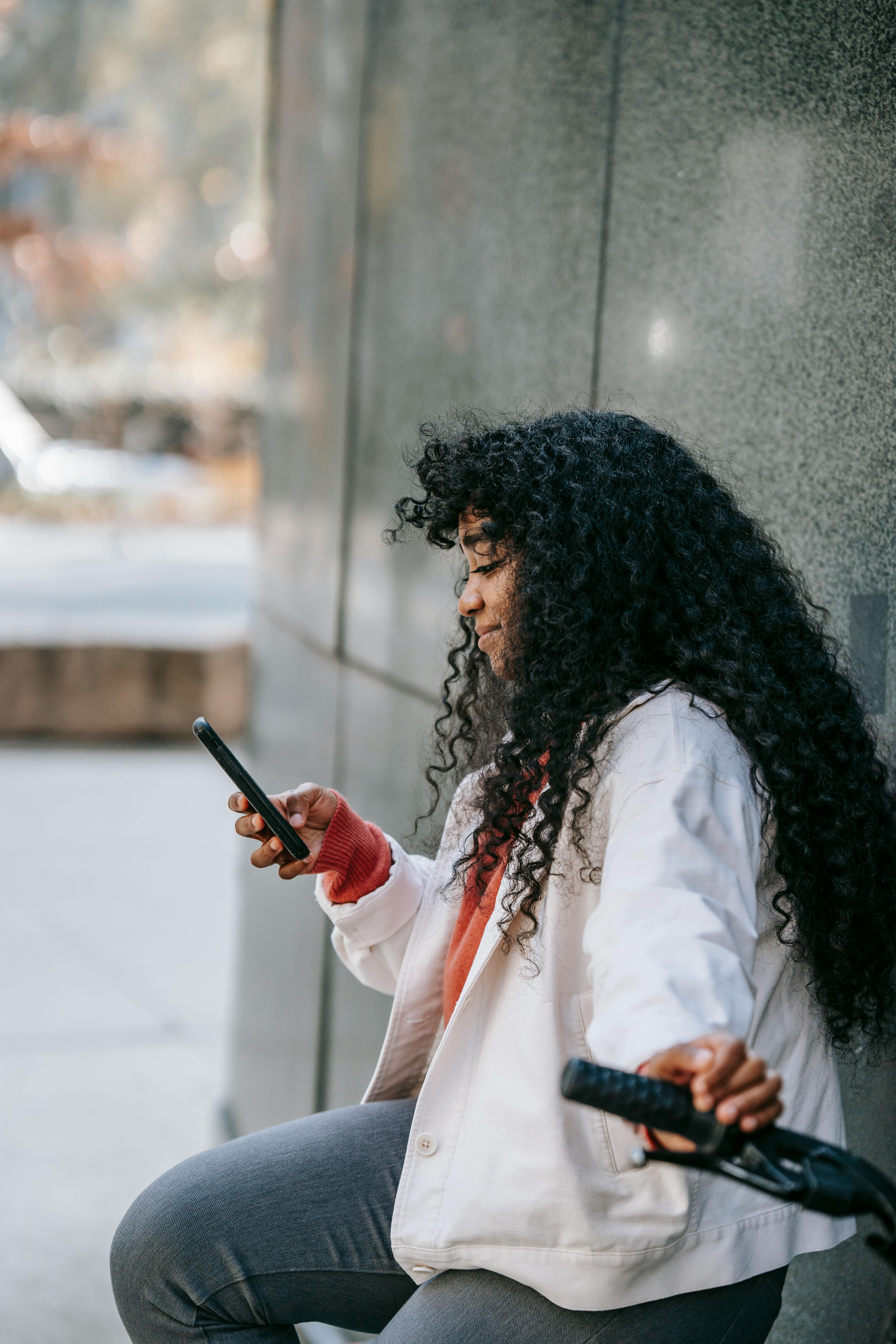 content black woman sitting on bicycle and browsing smartphone