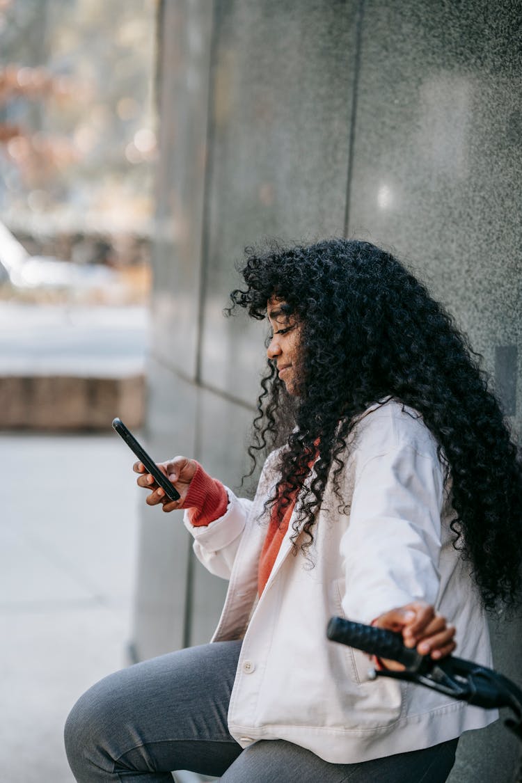 Content Black Woman Sitting On Bicycle And Browsing Smartphone