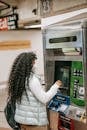 Back view attentive African American female with fine curly hair buying metro tickets via ticketing machine in underground hallway