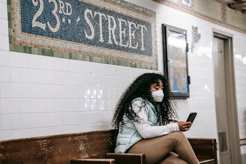 Focused African American female in casual clothes browsing mobile phone while sitting on bench in New York underground platform