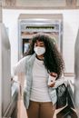 Thoughtful African American female in casual wear and face mask with takeaway coffee swiping ticket on turnstile in subway station