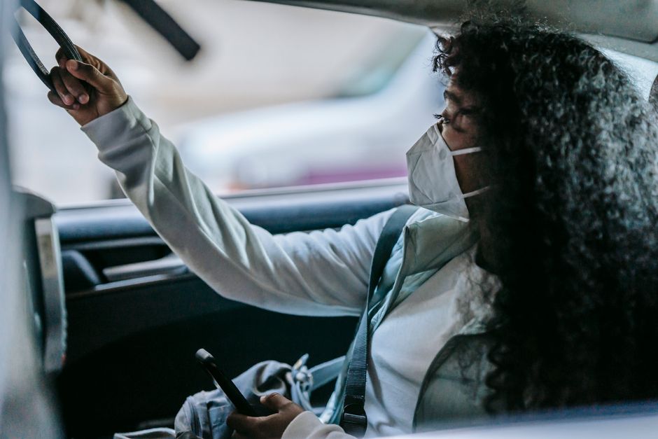 マスクを着用した考え込んでいる若い女性が車の後部座席に座り、電話に夢中になっています。