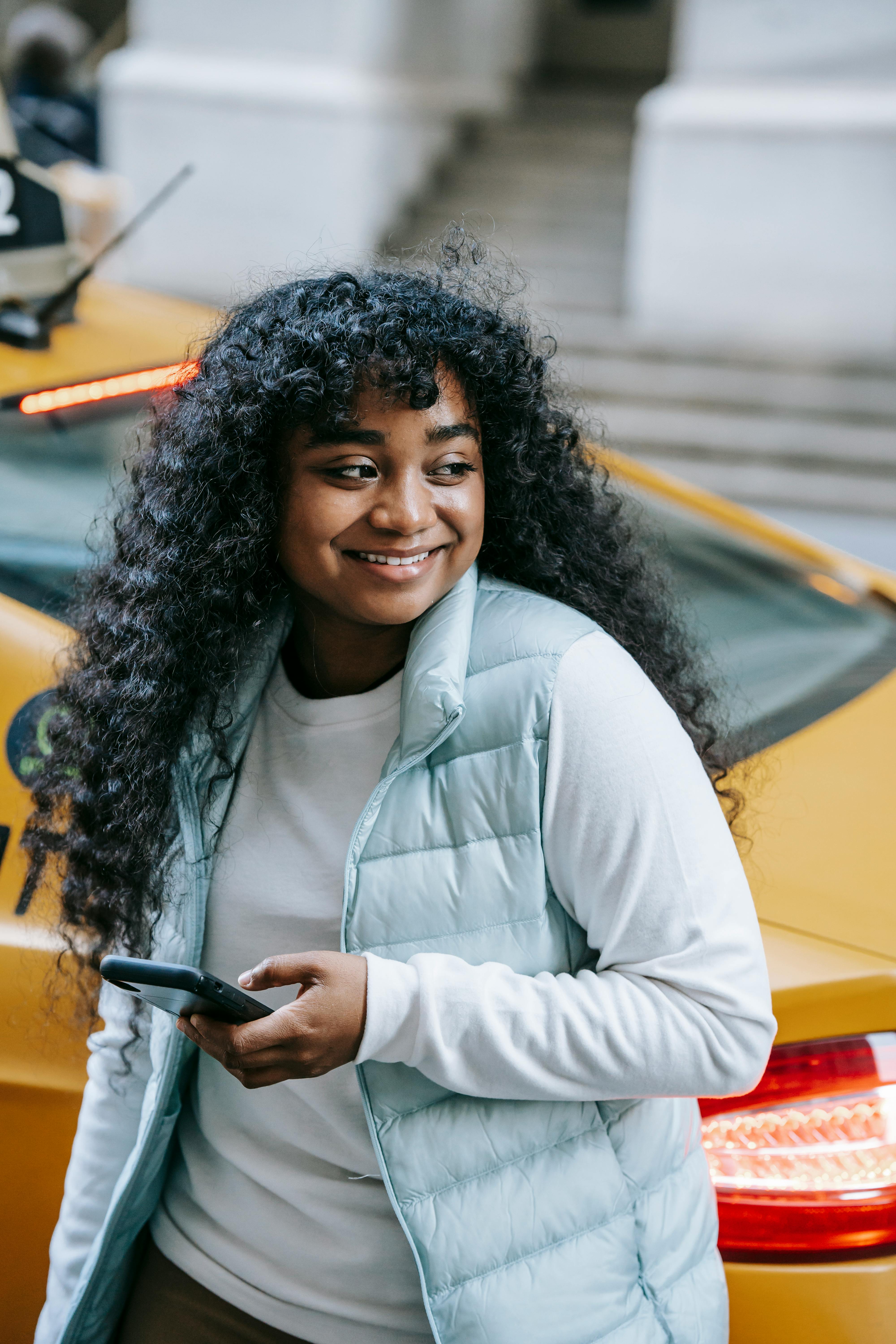 happy black female standing on street against taxi