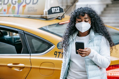 Black female with phone in mask near cab in city