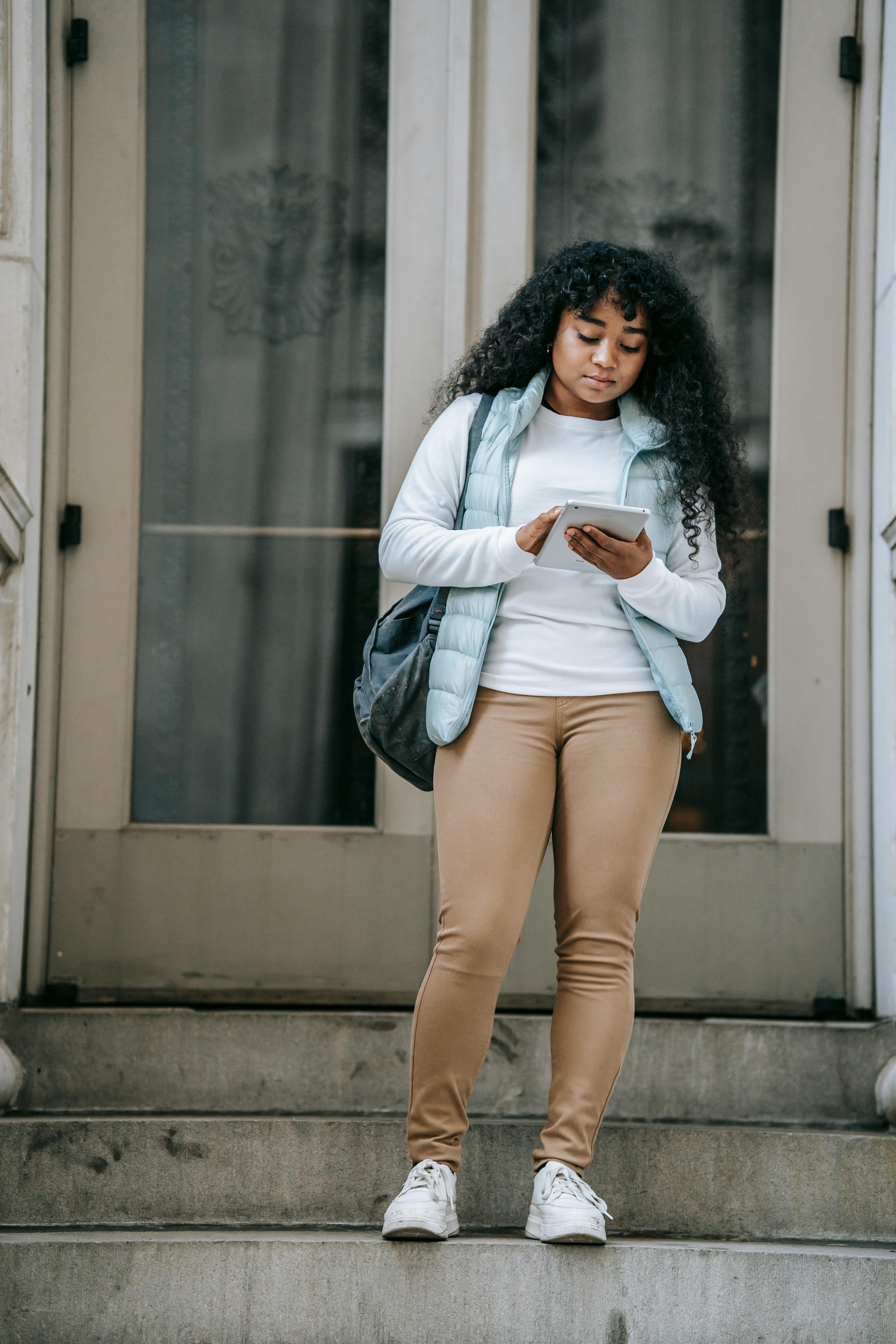 serious black lady browsing on tablet on steps near building