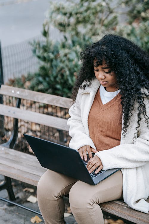 African American woman using netbook in park sitting on bench