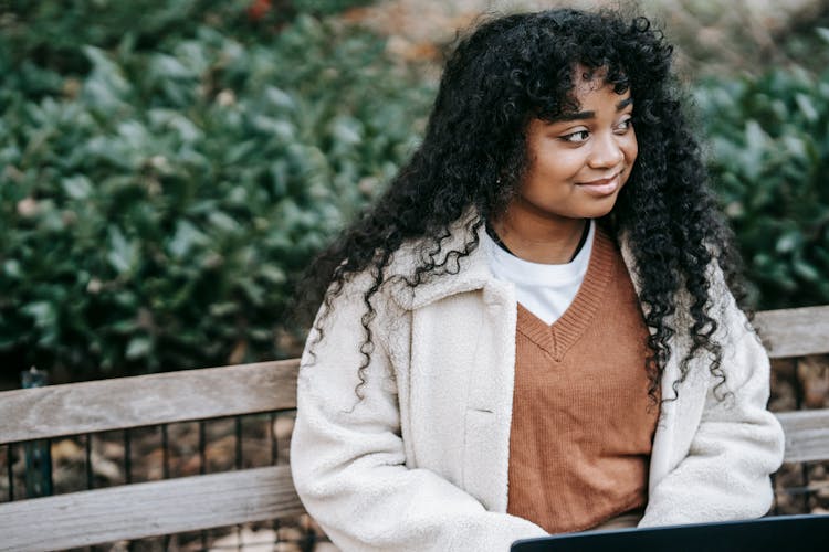 Smiling Black Woman With Laptop Sitting In City Park