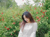 Woman in Beige Dress Standing Near the Green Plants with Red Flowers