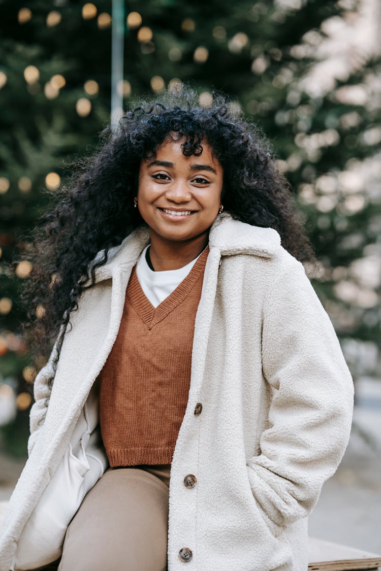 Pleasant Black Woman Standing Near Sparkling Christmas Tree On Street