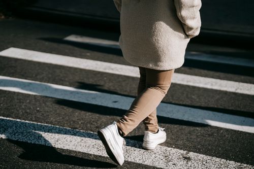 Free Back view crop unrecognizable female wearing casual outerwear crossing road on pedestrian crosswalk on sunny day Stock Photo