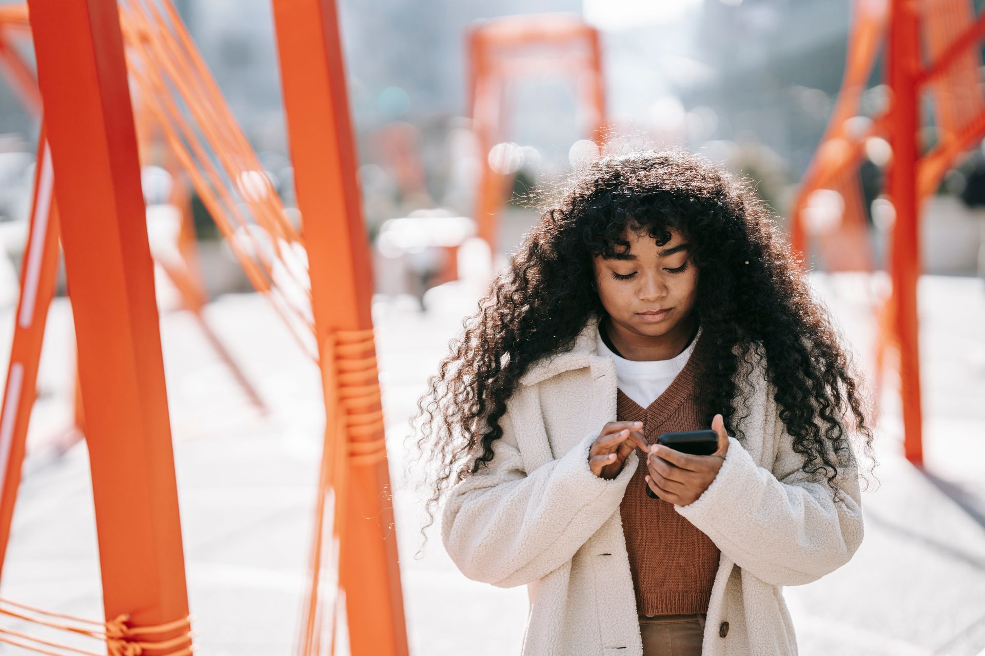 A young woman with curly hair using her smartphone outdoors on a sunny day.