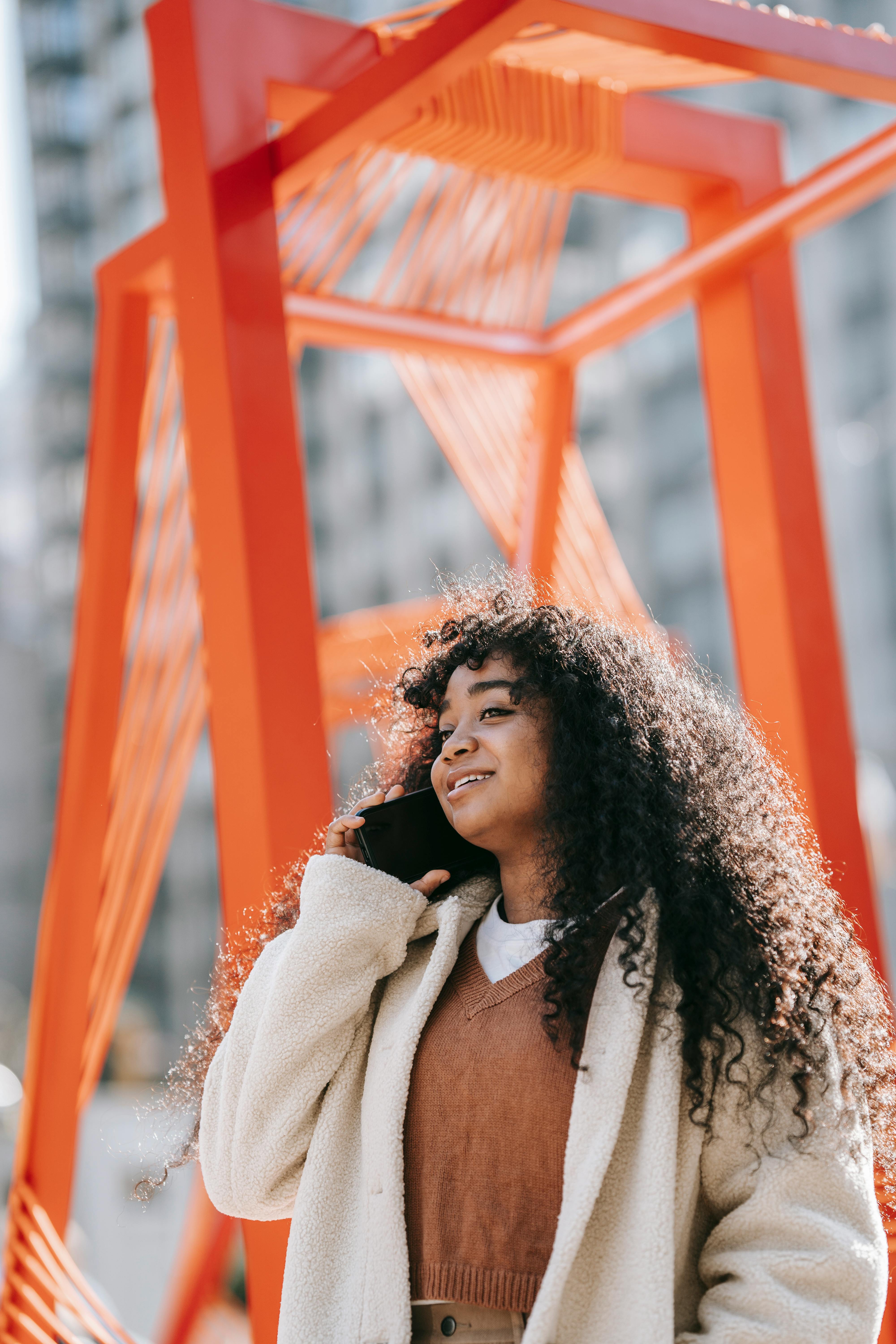 content black woman in outerwear talking on smartphone on street