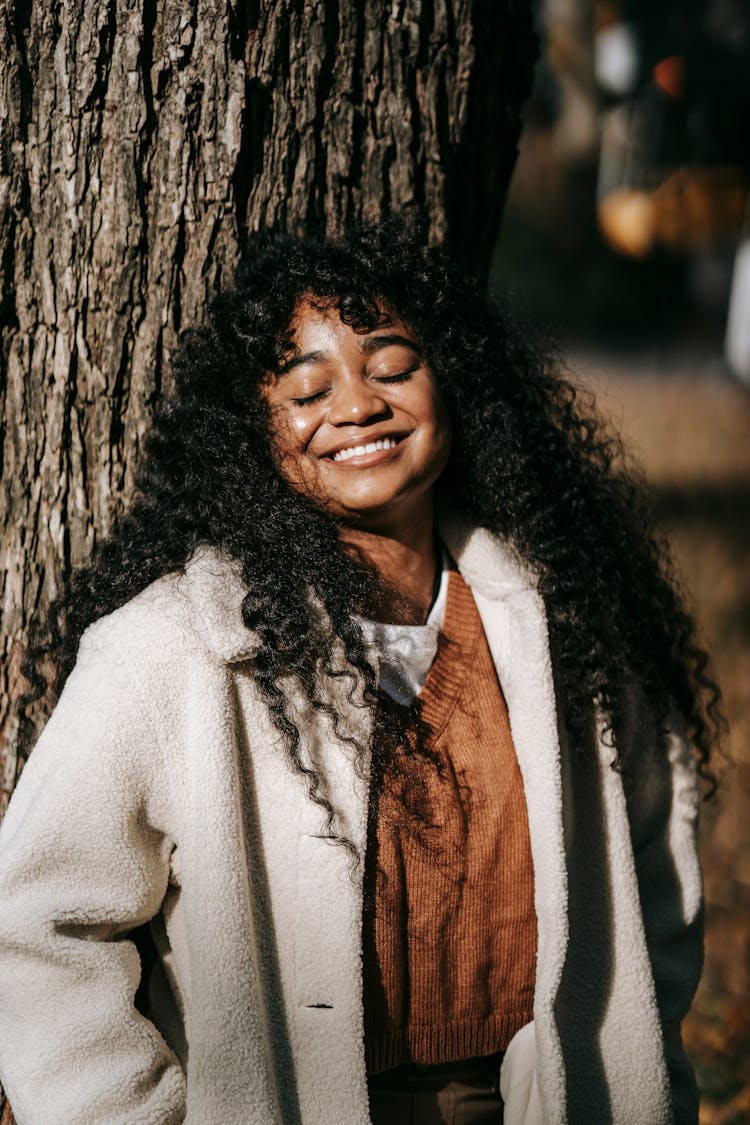 Smiling Black Woman Standing Against Tree In Spring Park