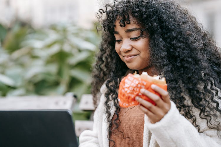 Content Black Woman With Burger Using Laptop In Garden