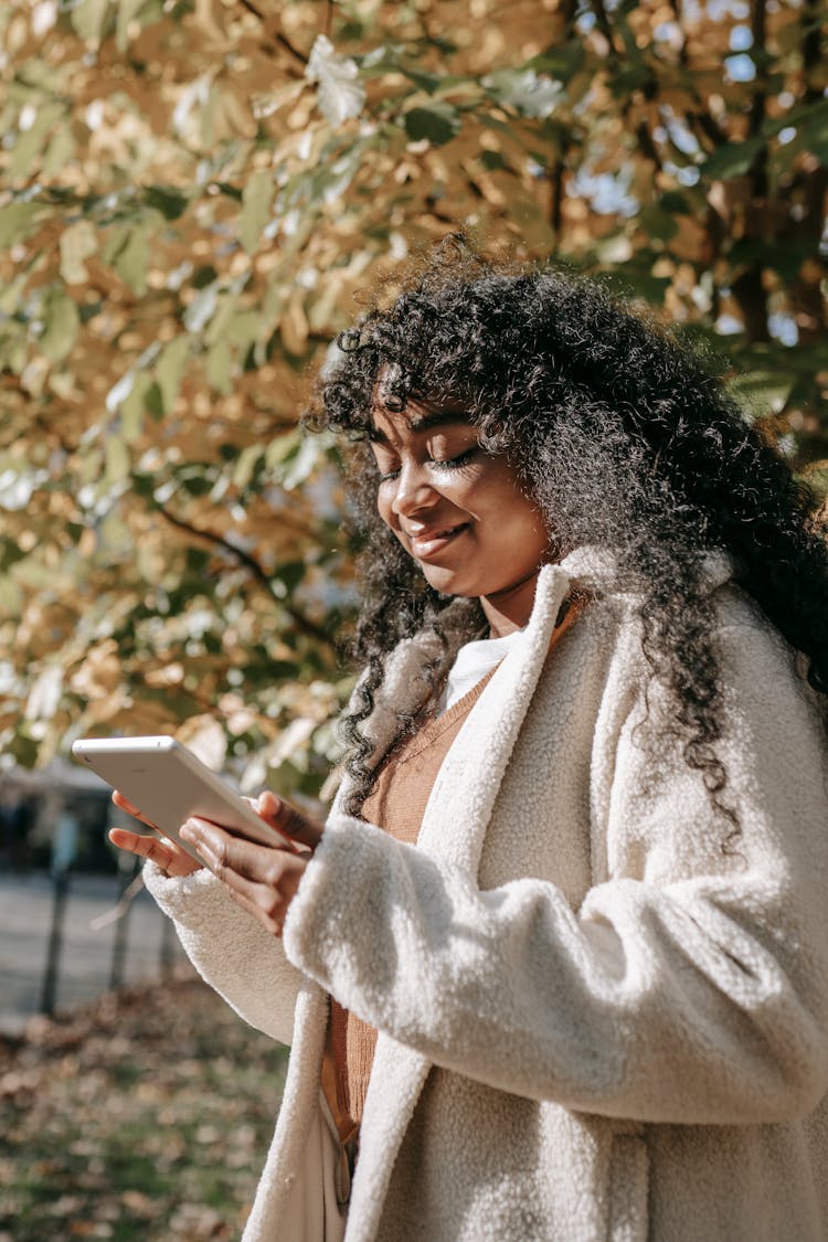 Smiling Black Woman Using Tablet In Sunny Autumn Park