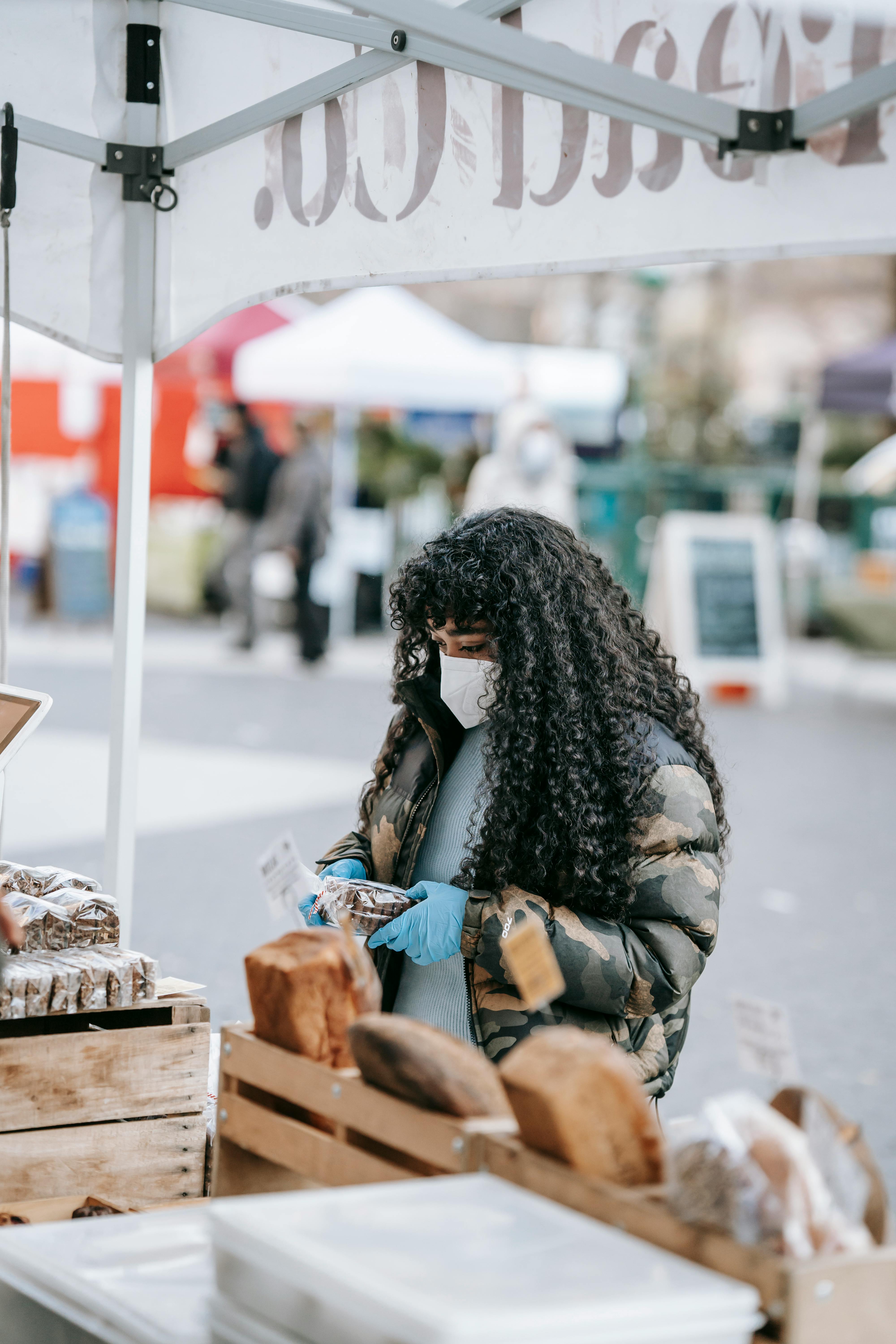 focused black woman in mask choosing goods in street market