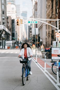 Full body of positive African American female with Afro hairstyle riding bike on asphalt road in megalopolis