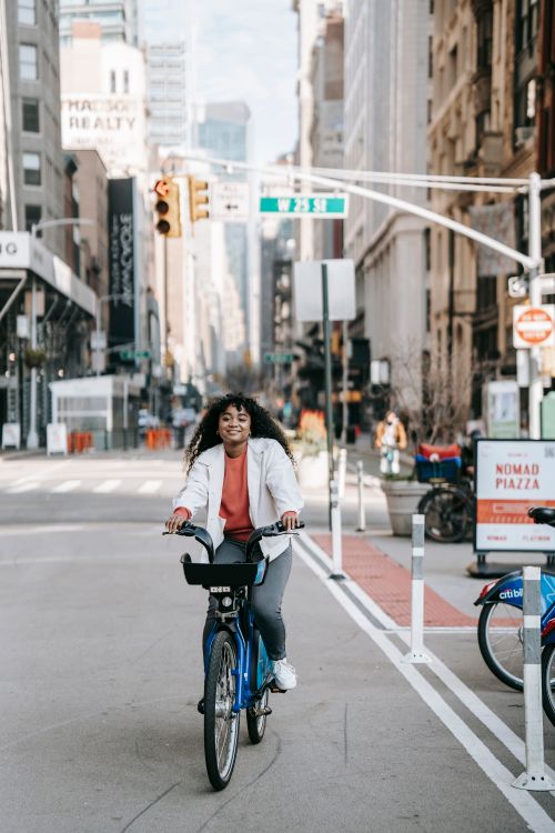Free Full body of positive African American female with Afro hairstyle riding bike on asphalt road in megalopolis Stock Photo