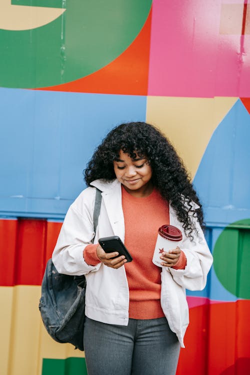 Free Smiling black woman using smartphone near colorful wall Stock Photo