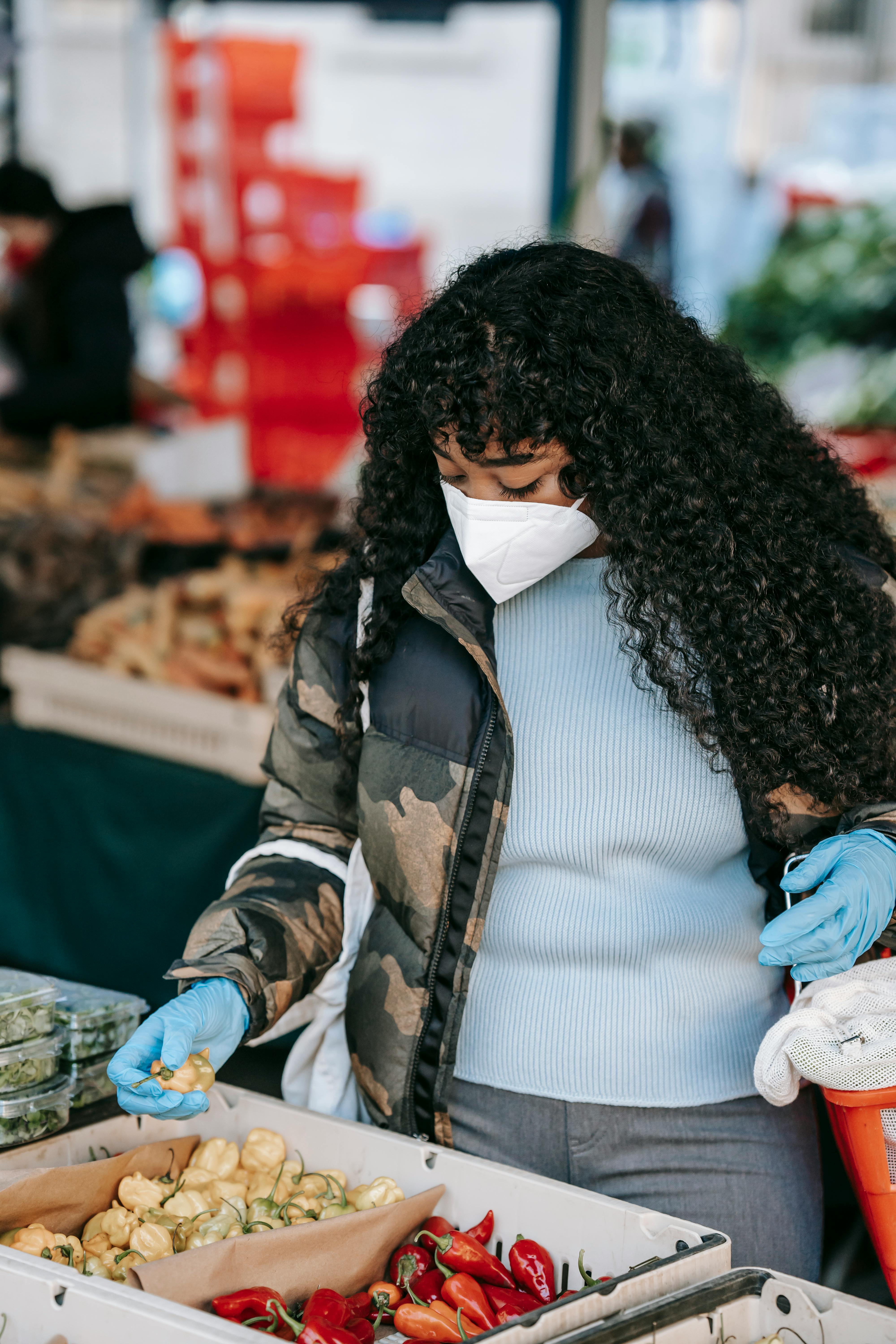 black woman in mask choosing vegetables in market