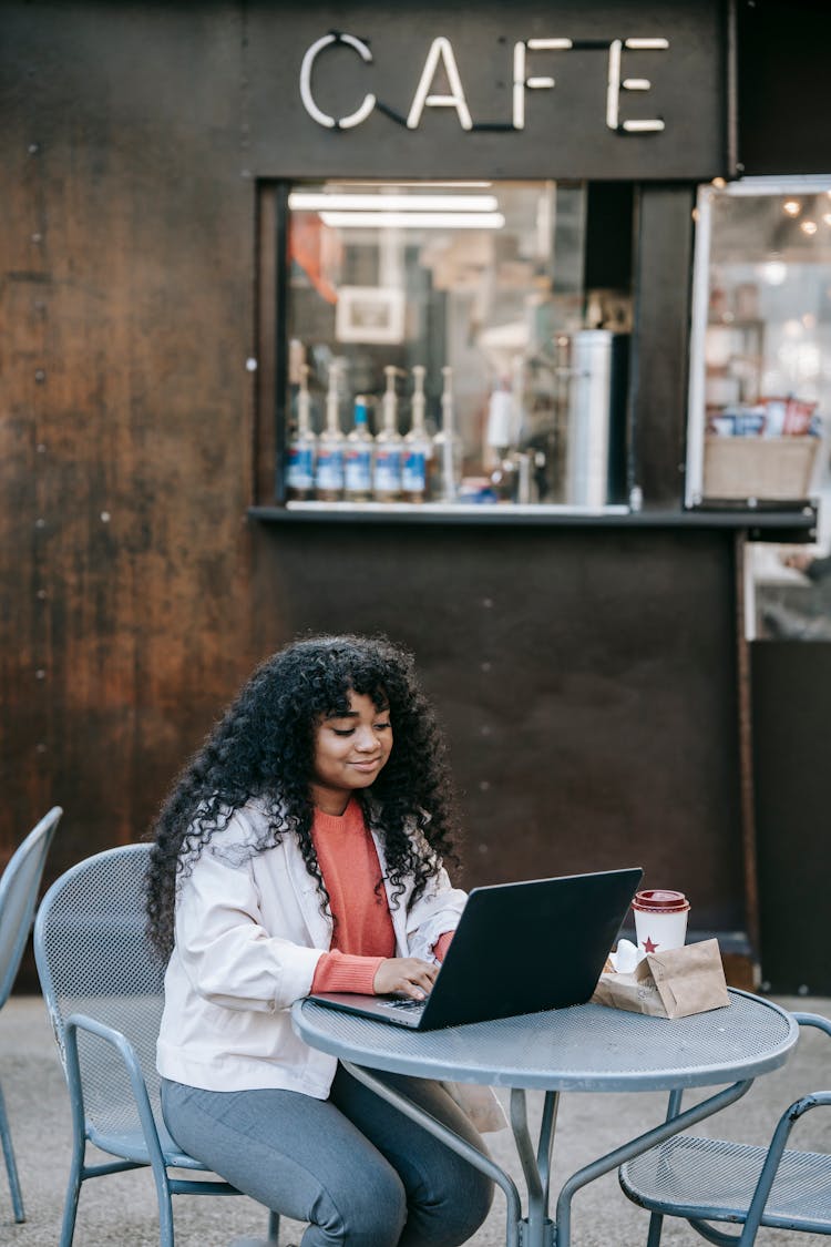 Cheerful Black Woman Browsing Laptop On Street Near Cafe