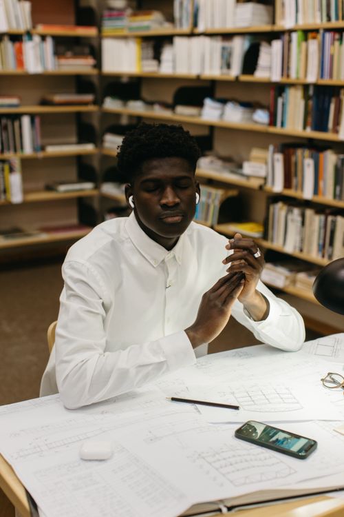 Free Adult student focusing on studies while listening to music with wireless earphones in a library. Stock Photo