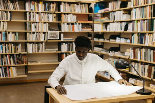 Free Architect reviewing blueprints in a library workspace, showcasing focused creativity. Stock Photo