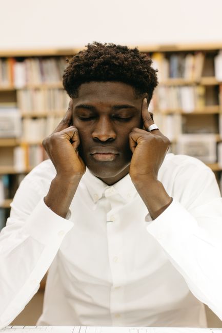 Man in white shirt concentrating in a library, eyes closed, with bookshelves in the background. Man in white shirt concentrating in a library, eyes closed, with bookshelves in the background.