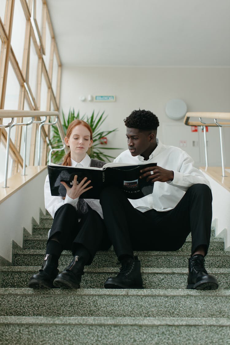 Man And Woman Sitting On The Stairway Reading A Book