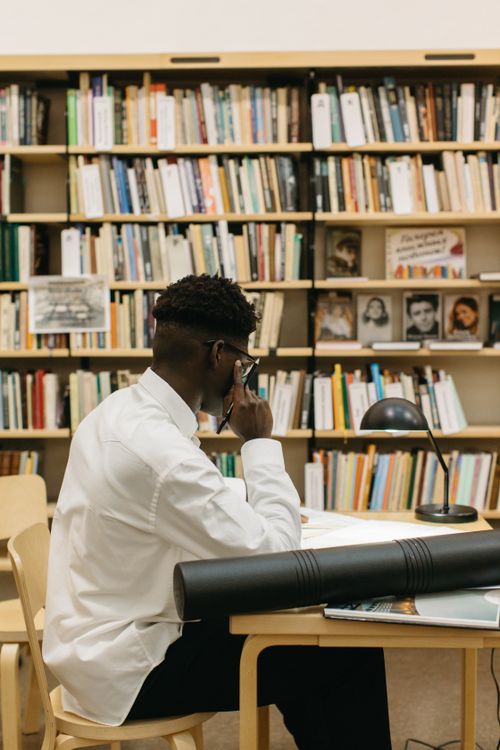 Free Dedicated architect immerses in study at a library desk, surrounded by books. Stock Photo