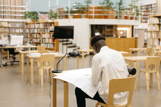 A student studying at a desk in a modern library with bookshelves and open space.