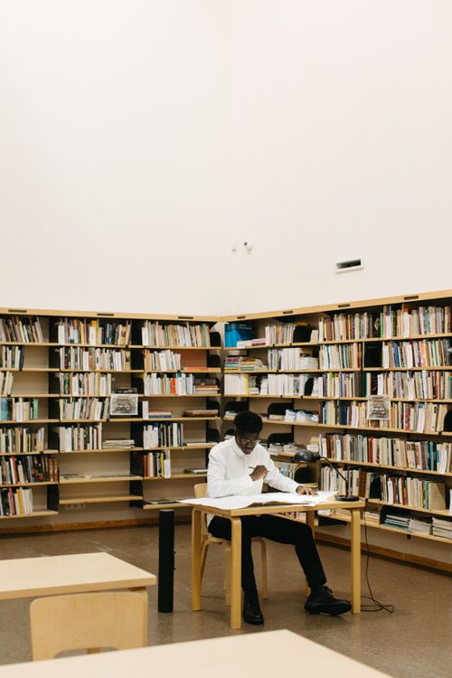 Free Man studying alone at a table in a bright, minimalist library with shelves full of books. Stock Photo