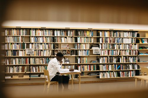 Free Adult man reading and studying in a well-lit library with bookshelves. Stock Photo