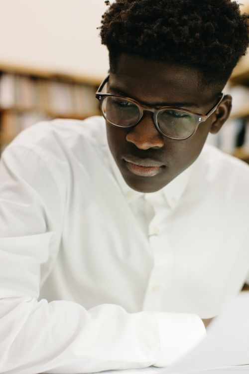 Free A young man deeply focused on study indoors, wearing eyeglasses and white shirt. Stock Photo