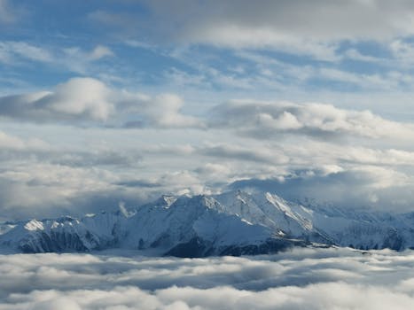 Stunning aerial shot of a snow-covered mountain range surrounded by clouds under a bright sky.