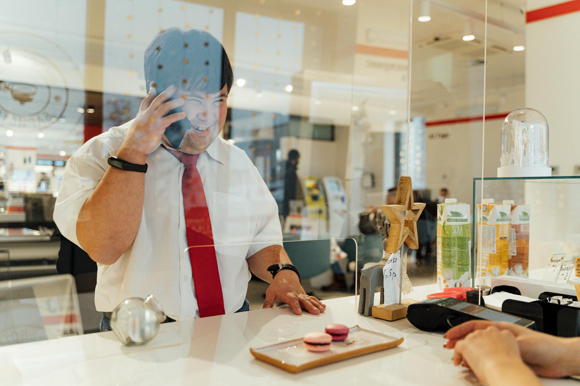 Smiling businessman chatting on phone behind a glass panel in a cafe.