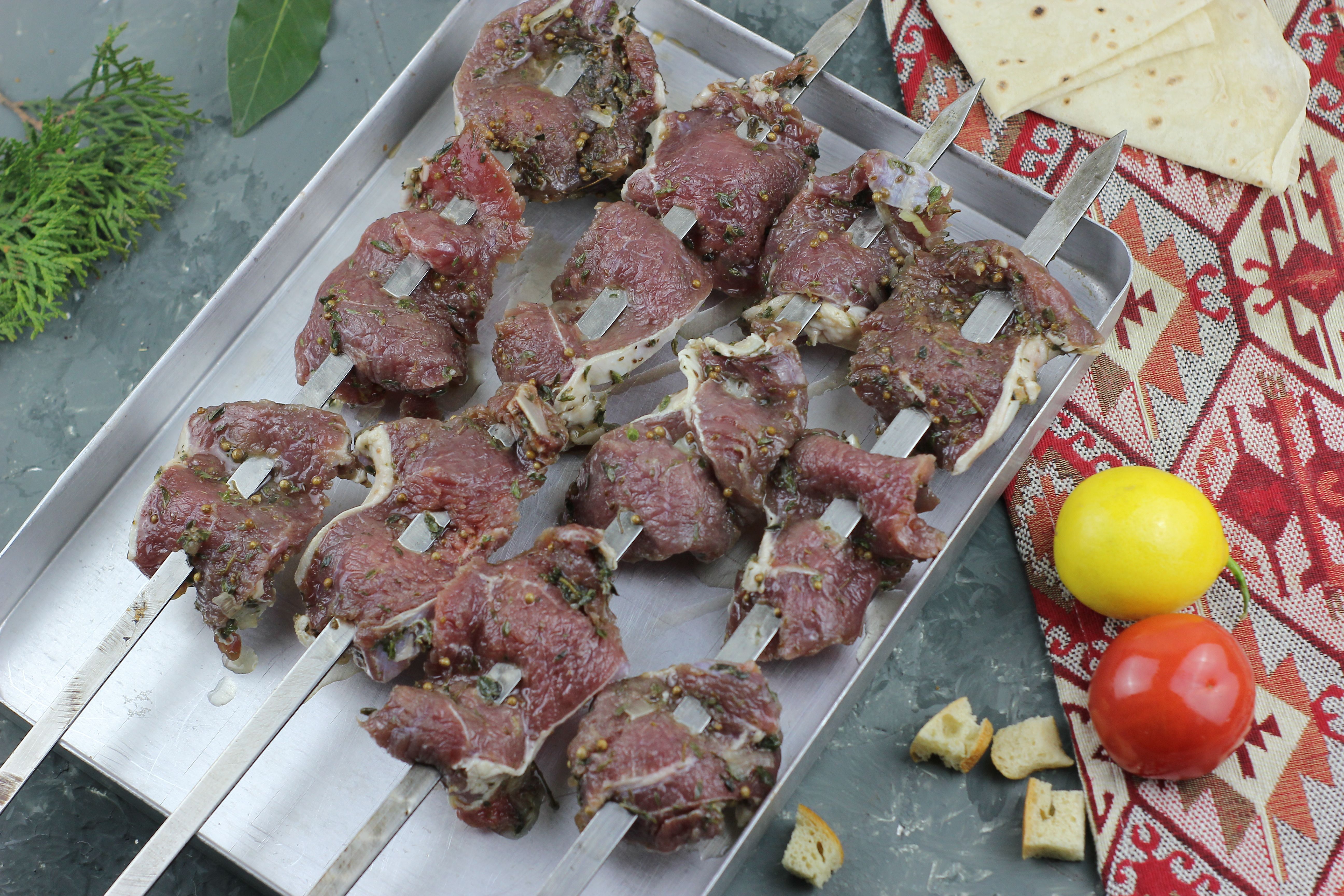 Freshly marinated meat skewers on a tray with tomatoes and spices ready for grilling.