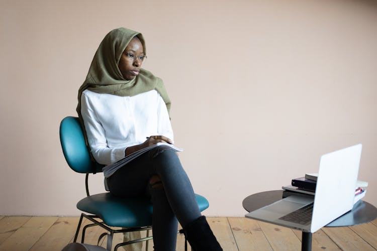 Black Muslim Woman Taking Notes And Watching Tutorial On Laptop