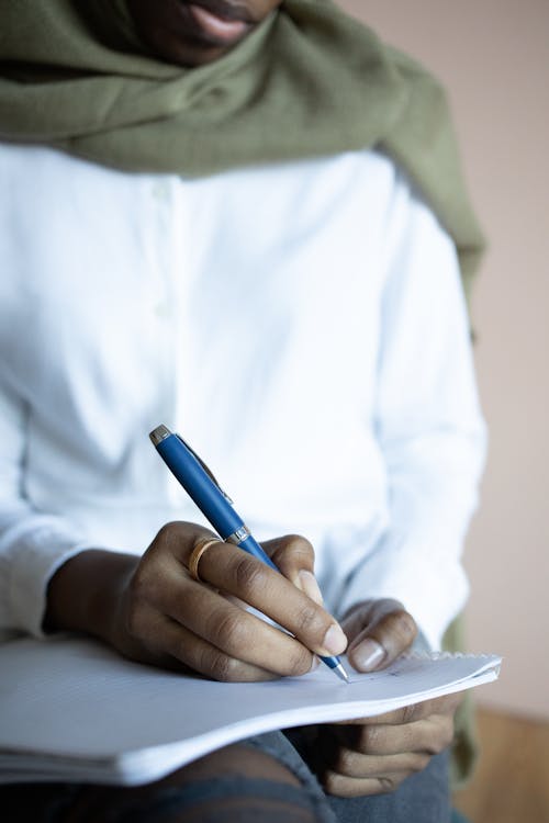 Crop black Muslim woman writing in copybook