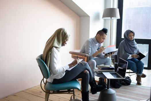 Focused multiethnic students writing in copybooks in coworking space