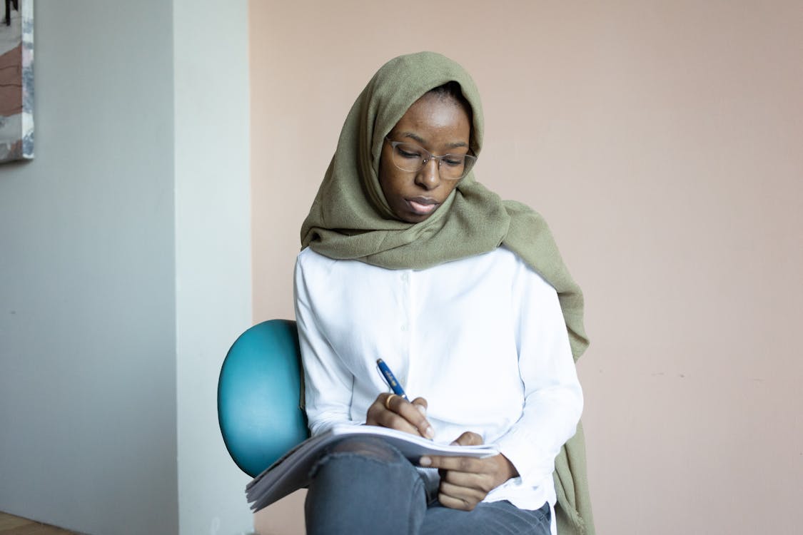 Serious black Muslim woman writing in notebook