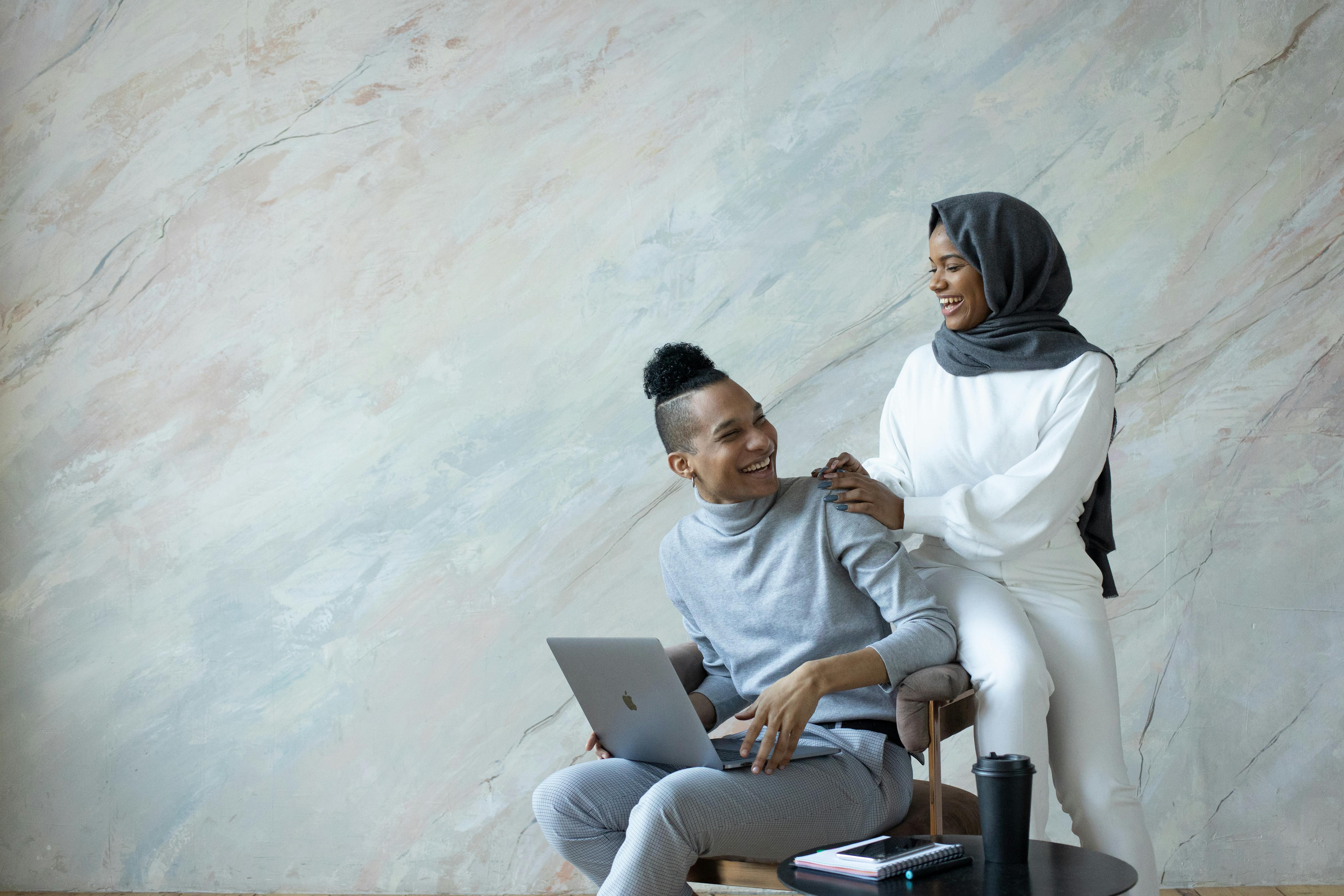 laughing ethnic couple browsing laptop on armchair