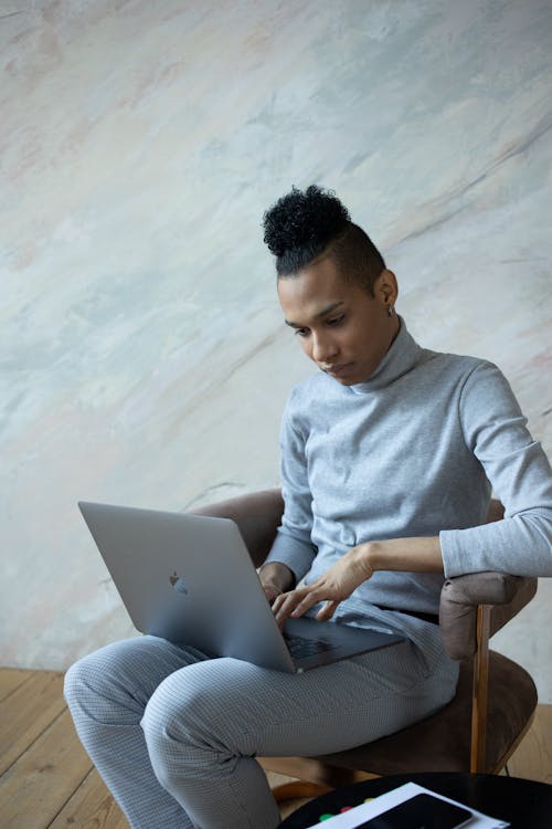 Free Serious African American male freelancer sitting on chair and typing on netbook while working online Stock Photo