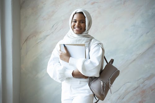 Positive Muslim woman with papers and backpack