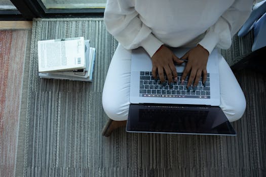 Top view of anonymous African American female student sitting with crossed legs and typing on netbook sitting near stack of books