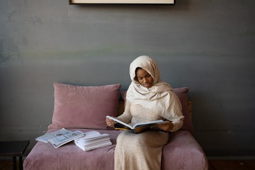 Serious black woman reading journal sitting on sofa