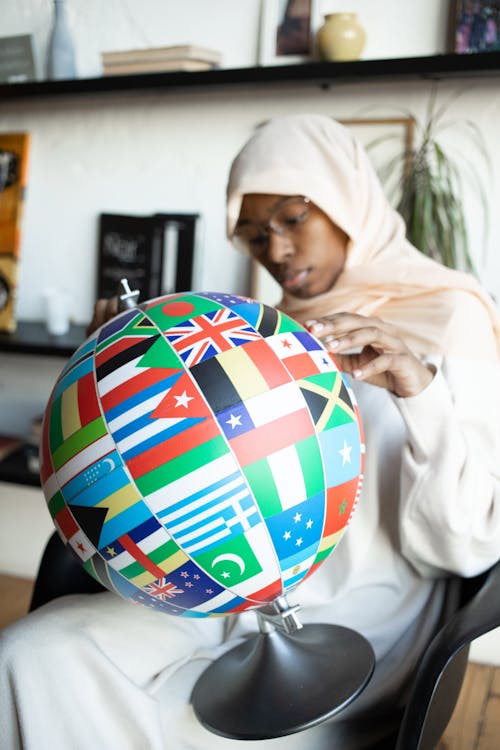 Concentrated African American female in traditional Muslim clothes and eyeglasses finding flag of country on globe